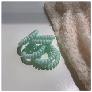Vue détaillée de quatre élastiques spirales vert menthe sur une surface blanche décorée