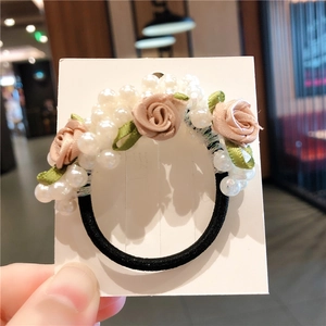 Détail de roses en tissu rose et perles sur un élastique à cheveux noir dans la main