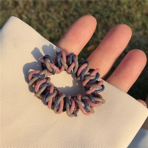 Détail d'un élastique spirale tissé tricolore pour cheveux tenu à la main