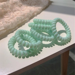 Élastiques à cheveux spirale vert menthe empilés sur table blanche avec dentelle