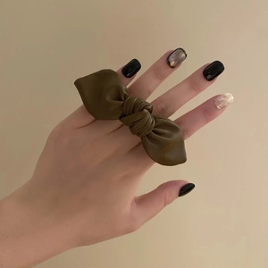 Detailed view of an olive green leather bow hair tie held in hand against a cream background