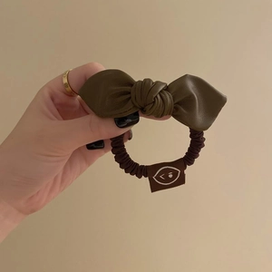 Detail of olive green faux leather bow hair tie with high-elastic dark brown cord