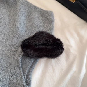 Gros plan sur une pince à cheveux noire en peluche sur un pull en maille grise