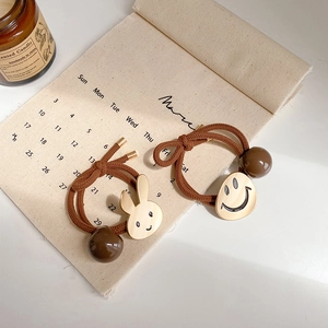 Detail van bruine haarelastiekjes met gouden konijn- en smiley-hangers op linnen basis