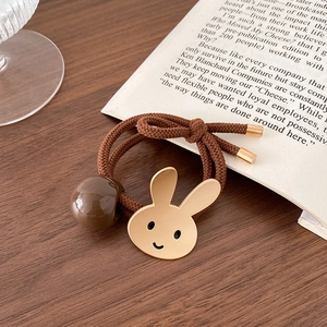 Detail van een bruine haarelastiek met een gouden Miffy-konijnhanger en glanzende kraal