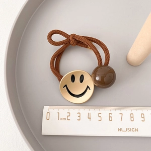 Detailopname van bruin haarelastiekje met gouden smiley-bedeltje en glanzende kraal