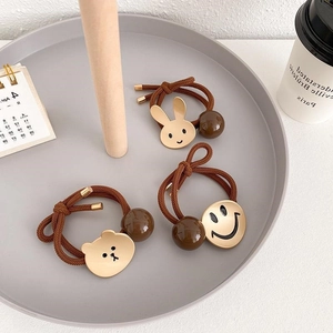 Driedelige set minimalistische haarelastiekjes met beer- en smiley-bedeltjes op dienblad
