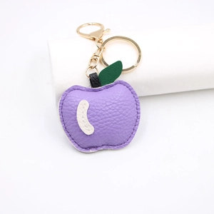 Detail of purple lychee pattern leather apple keychain with gold metal clasp and green leaf