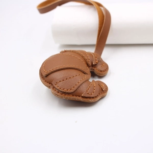 Detailed view of brown leather croissant charm with contrast stitching and long lanyard