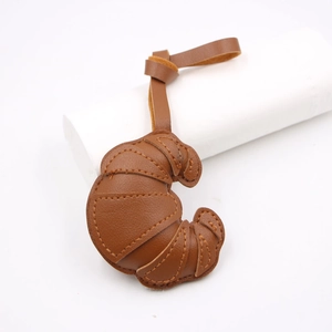 Close-up of brown leather croissant bag charm with layered stitching and matching strap