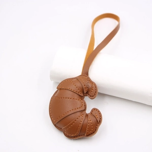 Close-up of brown leather croissant bag charm with detailed stitching and matching lanyard