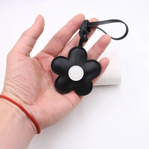Detail of hand holding a black leather cherry blossom flower pendant with white center