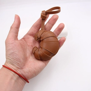 Close-up of caramel leather croissant bag charm with contrast stitching and litchi texture