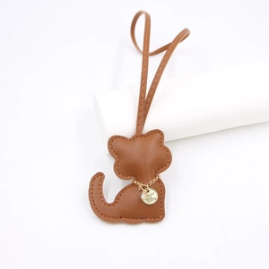 Detailed view of a brown leather cat bag charm with gold chain and engraved metal tag