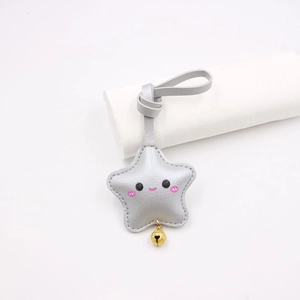 Close-up of a silver star-shaped leather keychain with a cute smiley face and golden bell
