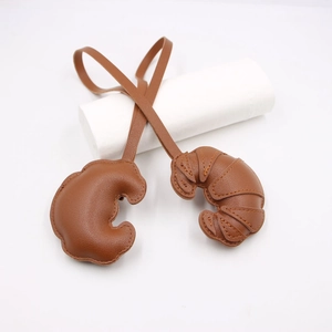 Close-up of brown leather croissant charms with detailed stitching and long lanyards