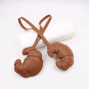 Detailed view of brown leather croissant-shaped charms with stitched layers and leather straps
