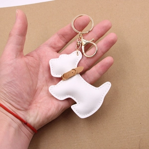 Handheld detail of a white leather Scottish Terrier charm with a brown collar and gold ring