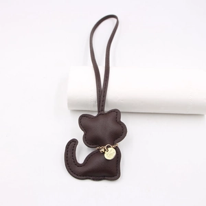 Detail of dark brown leather cat bag charm showing fine stitching and golden metal nameplate