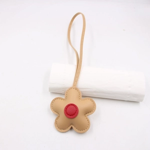 Close-up of a floral leather bag charm with cream petals and a red center detail