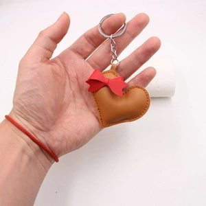Detail of brown leather heart keychain with red bow held in hand for scale