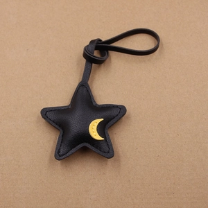 Detail of star-shaped black leather bag charm featuring a yellow moon and fine stitching