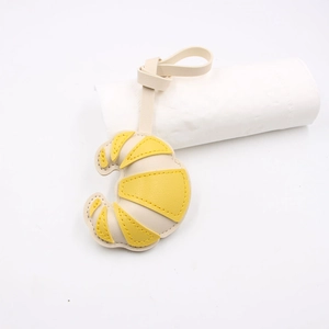Detail of a handmade croissant-shaped leather bag charm with yellow stitching and lanyard