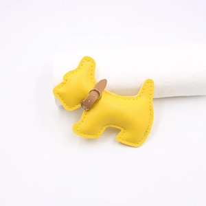 Detail of yellow leather dog-shaped bag charm with white stitching and metal buckle