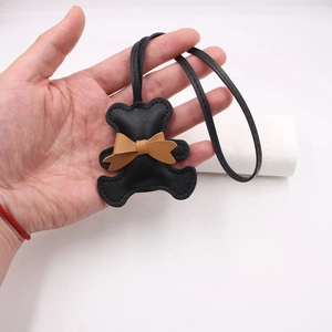 Close-up of black leather bear charm with brown bow and long strap accessory