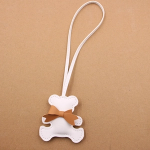 Detailed view of white leather bear charm with brown bow and litchi grain texture