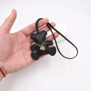 Close-up of black leather bear bag charm with gold chain detail held in hand
