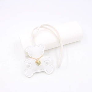 Close-up of white leather bear pendant with gold chain and engraved Love You metal tag