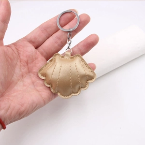Detailed close-up of golden leather shell keychain with metallic stitching held in hand