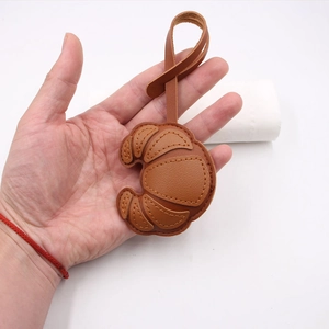 Handheld caramel leather croissant-shaped bag charm with matching strap and clasp