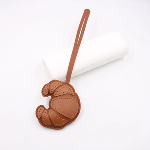Close-up of brown leather croissant bag charm with detailed stitching and long strap