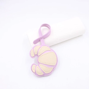Detail of croissant-shaped leather bag charm in purple and beige with fine stitching