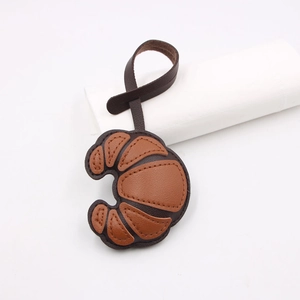Close-up of leather croissant bag charm showing premium litchi grain texture and stitching
