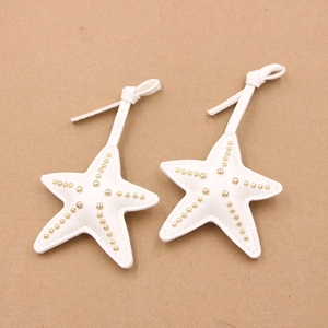Détail de deux breloques d'étoile de mer en cuir blanc avec rivets dorés et cordons
