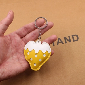 Detail of a handmade yellow strawberry leather keychain with white dots and silver ring