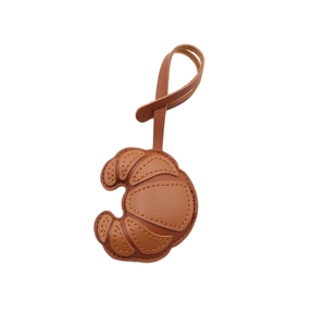 Brown leather croissant bag charm with detailed stitching and long matching strap