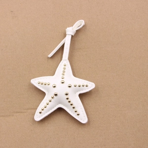 Détail d'un pendentif étoile en cuir blanc avec des clous dorés et des coutures apparentes