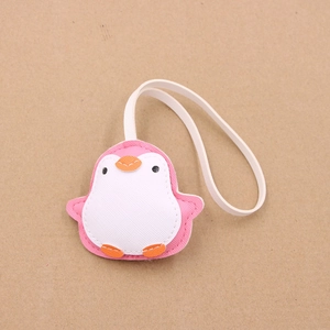 Pink faux leather penguin bag charm with white strap on a textured brown background