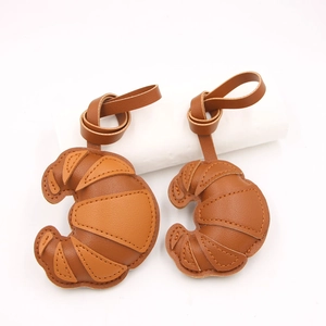 Detail eines übergroßen Croissant-Taschenanhängers aus Leder mit Kontrastnähten und Kordel