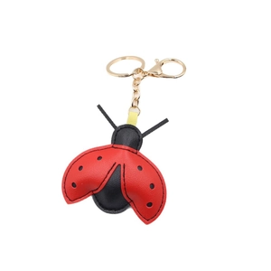 Ladybug shaped leather keychain with red wings and black polka dots on white background