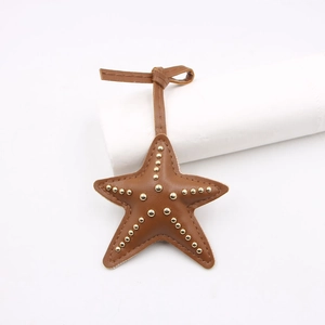 Détail d'un pendentif étoile de mer en cuir avec rivets dorés et coutures fines sur fond blanc