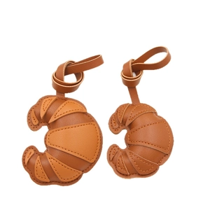 Zwei Taschenanhänger aus Leder im Croissant-Design mit minimalistischen Tragegurten
