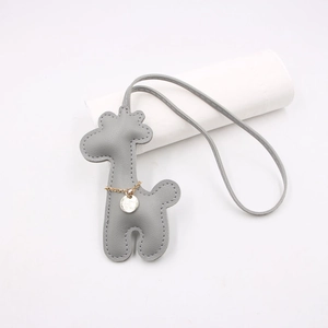 Detail view of a gray leather giraffe bag charm with elegant gold chain and metal tag accent