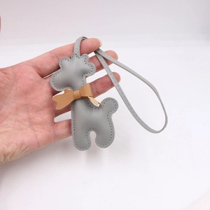 Pendentif de sac girafe en cuir gris avec nœud papillon tenu à la main sur fond blanc