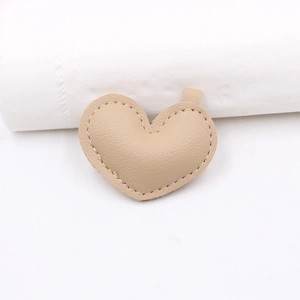 Dettaglio di ciondolo a cuore in pelle color crema con trama a grana e cuciture