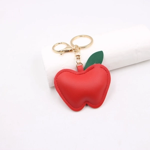 Red apple leather keychain with green leaf and golden metal hardware on white stand